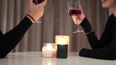 Romantik bir akşam yemeği. Evdeki mum ışığında romantik bir odada, siyah elbiseli güzel bir çift kırmızı şarap bardaklarını tokuşturuyor..