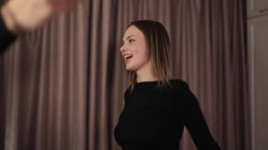 Güzel kız ve siyah elbiseli yakışıklı adam evde dans ediyor. Mutlu çift, erkek ve kadın gülüyor ve odada hareket ediyor..