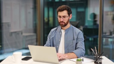 Modern ofiste dizüstü bilgisayarda çalışan başarılı bir iş adamı. Mutlu yönetici gözlüğü çıkarır ve kameraya gülümser. İş yerinde günlük gömlekli profesyonel bir işçi..