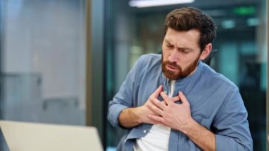 Ofisteki masasında çalışırken göğsünü ağrıtan endişeli iş adamı. Ani bir göğüs ağrısı, belki de kalp krizi geçiriyor..