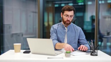 Modern ofiste çalışan odaklanmış bir işadamı dizüstü bilgisayardan video görüşmesi yaparken not alıyor. Şirket ortamında verimli iş günü.