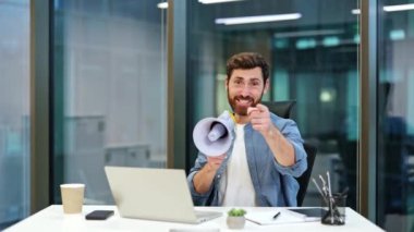 Megafonlu genç bir işadamı bir duyuru yapar ve parmağını kameraya doğrultur. Ofis çalışanı, ofis masasında oturan bir hoparlör kullanarak çalışanlarla yüksek sesle konuşur..