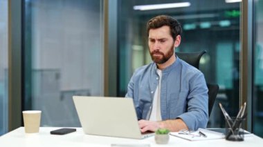 Hüsrana uğramış iş adamı, modern ofiste dizüstü bilgisayarla çalışırken kulaklarını elleriyle kapatıyor. Aşırı bilgi yoğunluğu ve stresten bunalmış..