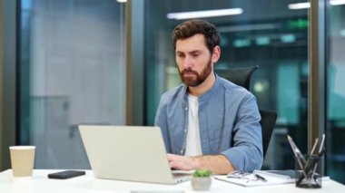 Sağlıksız iş adamı, modern ofiste dizüstü bilgisayarda çalışırken öksürüyor ve doku kullanıyor. Erkek çalışan hasta ve grip belirtileri gösteriyor..