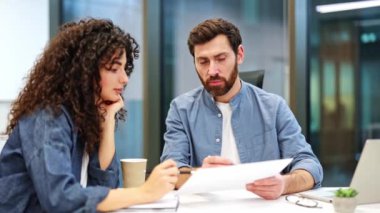 Odaklanmış meslektaşlar modern bir ofiste bir projeyi tartışıyorlar. İş adamı ve işkadını, takım çalışması ve profesyonelliği gösteren bir belge üzerinde işbirliği yapıyorlar..