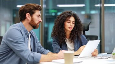 Kendine güvenen iş kadını, modern ofiste erkek meslektaşıyla evrak işlerini tartışıyor. Proje detayları üzerinde birlikte çalışıyorlar..
