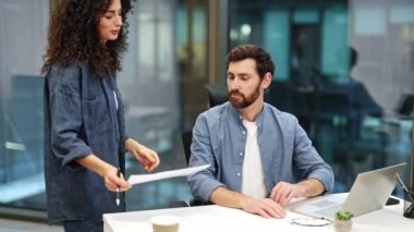 Odaklanmış meslektaşlar modern bir ofiste bir projeyi tartışıyorlar. İş kadını bir belgede bir iş adamına dizüstü bilgisayar kullanarak bilgi veriyor.