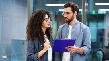 Kendine güvenen iş adamları modern bir ofiste bir projeyi tartışıyor. Biri bir pano tutarken, diğeri de takım çalışmasını ve işbirliğini gösteren bir kalemle işaret ediyor..