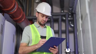 Ciddi, odaklanmış elektrik santrali işçisi panoya yazıyor. Erkek işçi kazan dairesini, ısıtma sistemi ekipmanlarını, boru hatlarını denetliyor. Konsantre mühendis, kazan dairesinde tesisatçı..