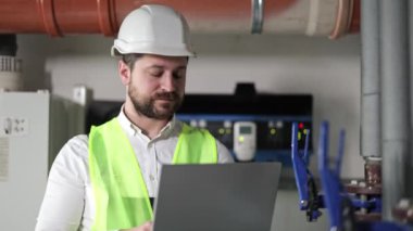 Kazan dairesinde sakallı, endüstriyel erkek işçi, çelik yelek ve çelik yelek giyiyor, bilgisayarın yanında ekipman kullanıyor..