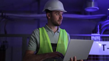 Elektrik odasında çalışan, çelik yelek ve çelik yelek giyen ciddi bir elektrik mühendisi. Bilgisayarı kullanan profesyonel bir adam elektrik santralinde çalışıyor..