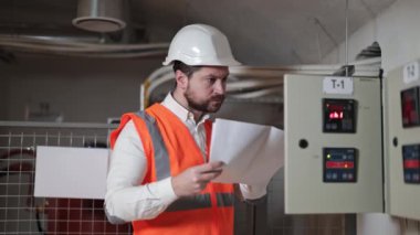 Ciddi elektrik mühendisi bir elektrik kontrol paneli ve belgelerini kontrol ediyor. Sunucu odasında çalışan endüstriyel elektrikçi. Kablolar ve dijital göstergelerle kontrol paneli.