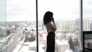 Karlı şehir manzaralı modern ofiste başarılı bir iş kadını telefonda konuşuyor. Şık bir çalışma alanında iş tartışan profesyonel bir kadın. Kendine güvenen kadın lider önemli bir karar veriyor..
