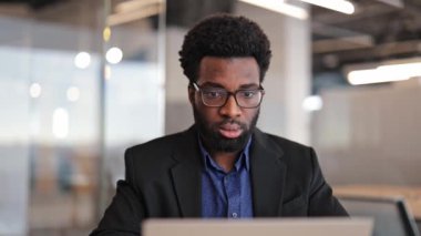 Modern ofiste dizüstü bilgisayarla çalışan odaklanmış Afro-Amerikan iş adamı. Düşünceli erkek serbest çalışan yönetici, takım elbiseli yönetici ve dizüstü bilgisayarla çalışan gözlüklü..