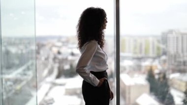 Karlı şehir manzarasına bakan kendine güvenen bir iş kadını. Profesyonel kadın kollarını kavuşturup şehir manzarasını izliyor..