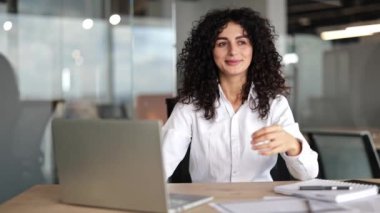 Kendine güvenen iş kadını modern ofiste meditasyon yapıyor. Kıvırcık saçlı, iş yerinde yoga egzersizi yapan rahat bir kadın. Sakin bir iş kadını işe ara veriyor. Stressiz iş kavramı.