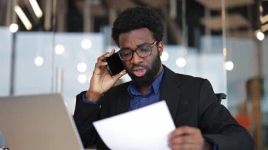 Odaklanmış işadamı önemli belgeyi telefon yoluyla tartışıyor. Modern ofiste çalışan profesyonel bir adam. Teknolojiyle birden fazla iş yapan verimli bir şirket çalışanı..