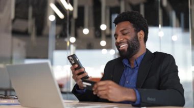 Neşeli genç Afrikalı işadamı akıllı telefondan online ödeme yapıyor. Modern ofis ortamı. Siyah erkek girişimci internetten alışveriş yapıyor..