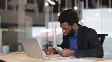 Confident young businessman counting money at his modern office desk. Successful entrepreneur managing finances, calculating profit. Corporate lifestyle.