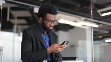 Modern ofiste akıllı telefon kullanan odaklanmış bir işadamı. Cep telefonundan mesaj atan gözlüklü, takım elbiseli, kendine güvenen bir erkek..