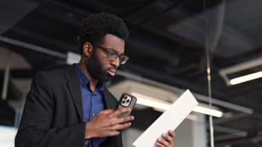 Telefon kullanarak ve belgeleri analiz ederek odaklanmış bir işadamı. Modern ofiste evraklarla çalışan düşünceli bir erkek girişimci. Takım elbiseli başarılı adam raporunu okuyor..