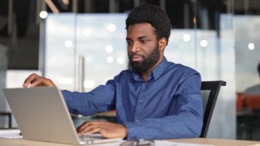 Başarılı genç iş adamı laptopta işini bitirir, onu kapatır ve rahatlamak için ofis sandalyesine yaslanır..
