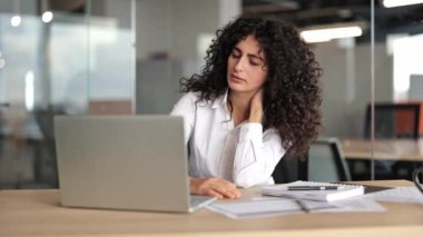Yorgun iş kadını boynu ovuşturuyor. Rahatsızlık duyuyor. Modern ofiste uzun bilgisayar çalışmalarından sonra acı çeken bitkin kadın işçi..