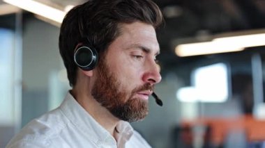 Modern ofisteki müşteriye kulaklık takmış odaklanmış iş adamı. Profesyonel müşteri hizmetleri ya da teknik destek sağlayan sakallı adam..