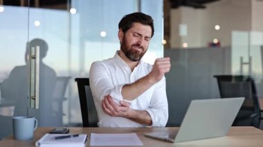 Dizüstü bilgisayar üzerinde çalışırken dirsek ağrısı çeken konsantre bir iş adamı. Erkek, dirsek ağrısı çekiyor. Ofisteki masasında oturan bir iş adamı. Çalışan adam.