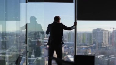 Endişeli iş adamı, soğuk kış günlerinde güzel şehir manzaralı modern ofiste perdeleri açar ve telefonda konuşur..