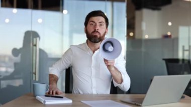 Kızgın işadamı ofis masasında megafona bağırıyor. Öfkeli erkek patron bağırır ve işyerini işaret eder. Stresli yönetici işyerindeki çalışanları azarlıyor.