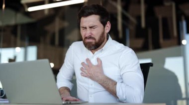Stresli iş adamı ofiste göğüs ağrısı çekiyor. Yorgun erkek işçi işyerinde kalp krizi geçiriyor. Modern ofiste acı çeken yorgun bir adam..