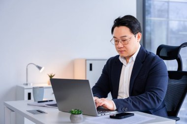 Asyalı Koreli iş adamı modern bir ofiste dizüstü bilgisayarla çalışıyor. Odaklanma ve kararlılıkla profesyonel çevre. Spor ceket giyip, başarılı bir iş yeri sergilemek..