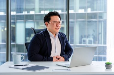 Modern ofiste kendine güveni tam bir iş adamı sanal bir toplantı yapıyor, profesyonellik ve pozitiflik yayıyor, düzenli bir masada oturuyor..