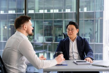 Profesyonel meslektaşlar zarif bir modern ofis ortamında iş konularını tartışırlar. Atmosfer üretkenliği, işbirliğini ve anlayışlı konuşmayı, takım çalışmasını yansıtır..