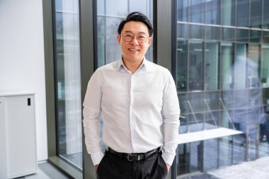 Çağdaş bir ofis binasının penceresinin yanında, şık giyinmiş, kendine güveni ve yaklaşımı olan başarılı bir profesyonel..