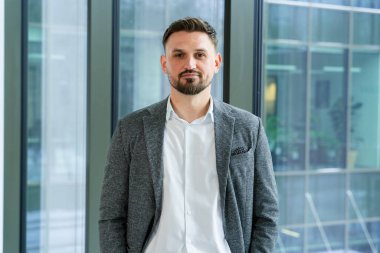 Modern bir ofis ortamında şık bir takım elbise giyen profesyonel ve kendine güvenen işadamı, kurumsal ve odaklanmış bir tavır sergiliyor..