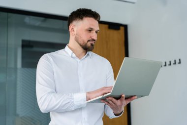 Modern ofis ortamında dizüstü bilgisayarla çalışan başarılı bir iş adamı, odak ve kararlılığını iletiyor. Sahne, çağdaş bir çalışma alanında üretkenlik ve profesyonelliği öneriyor.