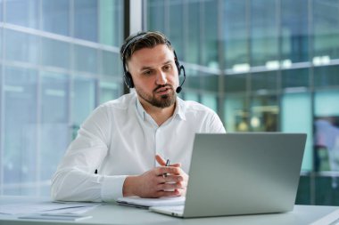 Çevrimiçi bir toplantıda çalışan, modern cam bir binada çalışan kendine güvenen bir iş adamı. Gündüz vakti gösterişli bir ofis ortamında profesyonel iletişim gösterme.