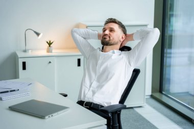 Modern ofisteki kendine güvenen iş adamı ofis koltuğuna oturmuş, tatmin olmuş ve profesyonel görünüyor. Şık ve iş odaklı giysiler modern mekânda görünümü tamamlıyor.