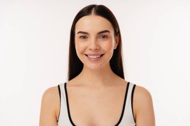 Beyaz stüdyo arka planında doğal bir gülümseme ve sakin bir ifade sergileyen kadın model..