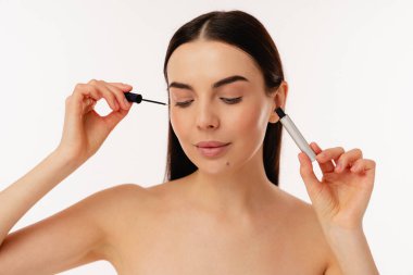 Individual using a mascara wand for applying makeup, showcasing a natural and elegant facial look. clipart