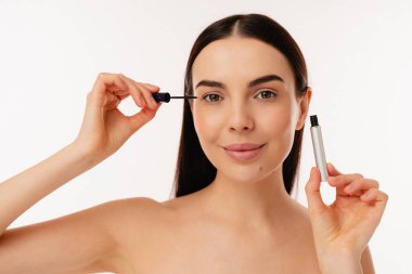 Tarafsız bir arkaplana karşı doğal güzellik ve makyaj tekniklerini vurgulayarak rimel sürmeye hazırlanan bir bireyin portresi.