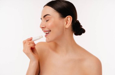 Dudak kremi kullanırken gülümseyen, kendine özen gösterme konseptini sergileyen ve cilt bakımını ve günlük rutinlerini geliştirmek için ürünleri teşvik eden bir kişinin yakın çekimi.