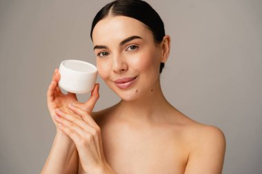 Individual with flawless skin holding a white jar, emphasizing self-care, beauty, and softness. clipart