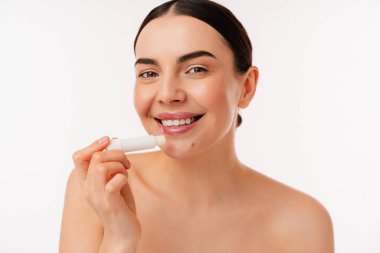 Gülümseyen, dudak kremi süren, cilt bakımını ve sağlıklı dudaklar için kişisel bakım rutinlerini temsil eden bir kadın model..