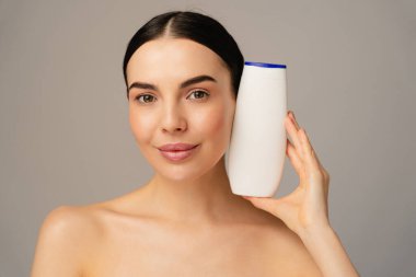 Beyaz plastik bir şişe tutan bir kadının portresi, kozmetik ürünleri veya kişisel bakım ürünlerini sembolize ediyor. Dekor, minimalist bir altyapı ve doğal güzellik ve cilt bakımı içeriyor..