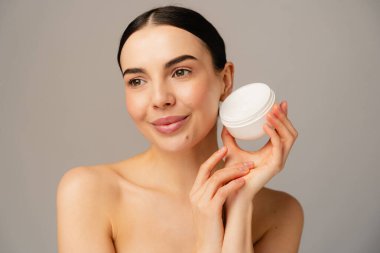 Cilt bakımı yapan, sağlıklı yaşam tarzını ve cilt bakım ürünlerini destekleyen gülümseyen bir insanın yakın plan portresi. Görüntü doğal güzelliği ve kişisel bakım temalarını tarafsız bir arkaplanda yakalıyor..