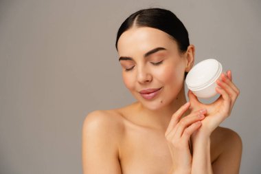 Modellik yapıyor ve bir kavanoz cilt kremi sunuyor. Huzurlu bir gülümsemeyle. Güzellik, sağlık ve kişisel bakım için harika..