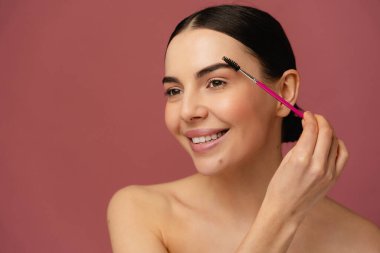 Kişisel bakım ve güzellik uygulamalarını tasvir eden, pembe bir arkaplan üzerine kurulmuş, neşe saçan bireysel kaşların yakın çekimi..